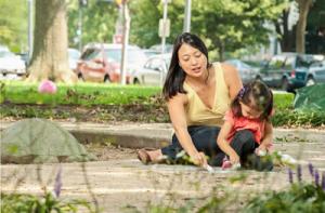 Photo of woman and child playing with sidewalk chalk.