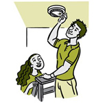 A man and a woman, the man changeing a smoke detector.