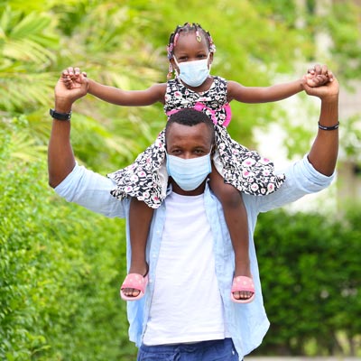 man holding his daughter on his shoulders while they both wear masks